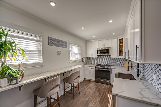 kitchen featuring stainless steel appliances, light stone counters, white cabinetry, and a kitchen breakfast bar