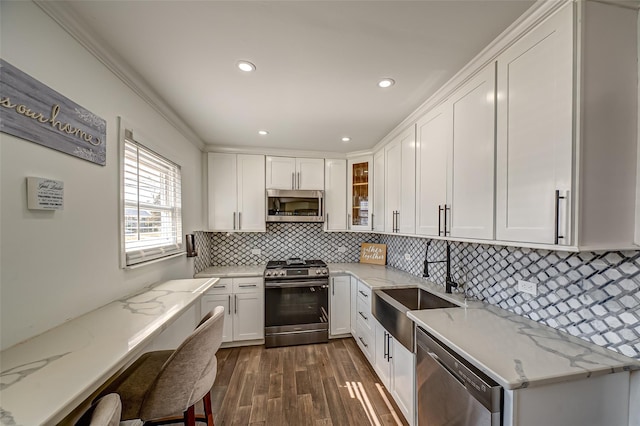 kitchen with light stone counters, stainless steel appliances, glass insert cabinets, white cabinetry, and a sink