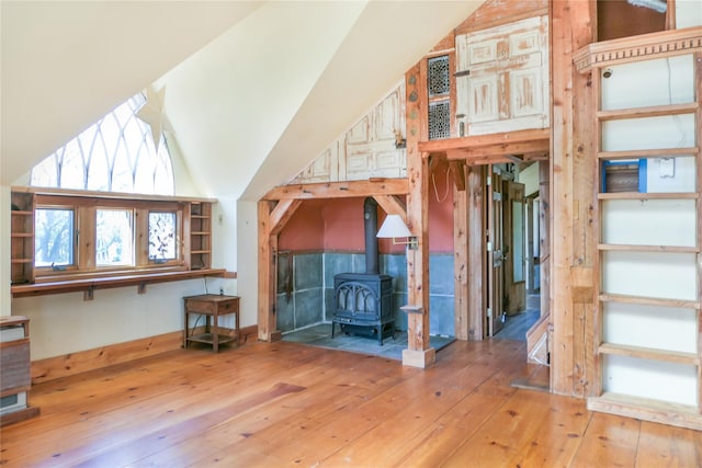 unfurnished living room featuring high vaulted ceiling, a wood stove, and hardwood / wood-style floors