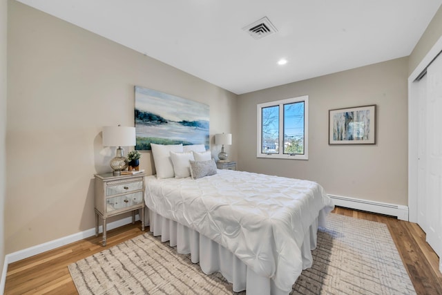 bedroom featuring baseboards, visible vents, baseboard heating, and wood finished floors