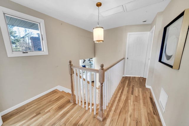 hall with light wood-style floors, baseboards, and an upstairs landing