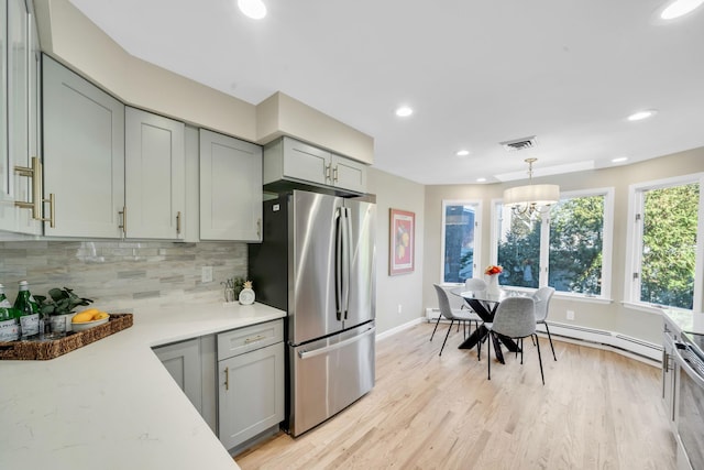 kitchen with a baseboard radiator, light wood-style flooring, light countertops, freestanding refrigerator, and tasteful backsplash