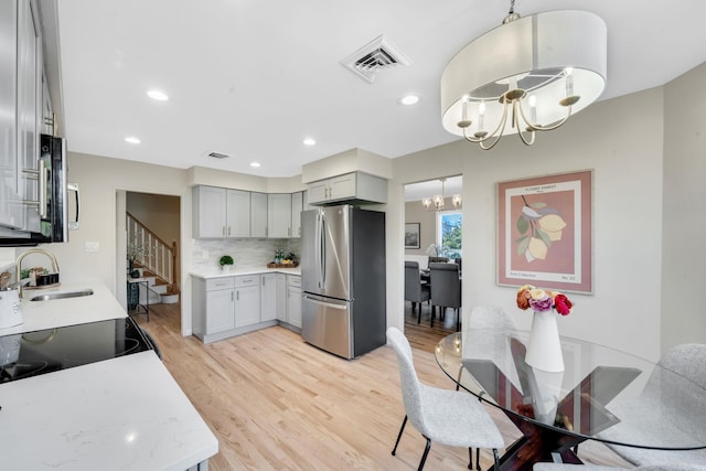 kitchen featuring gray cabinetry, a notable chandelier, a sink, visible vents, and freestanding refrigerator