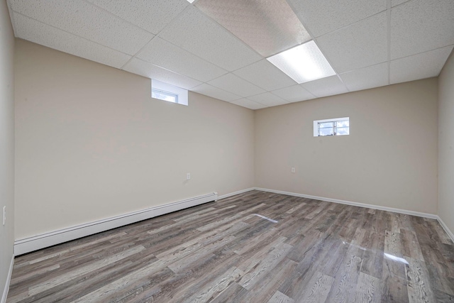 basement with a baseboard radiator, a drop ceiling, baseboards, and wood finished floors