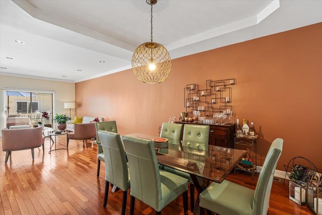 dining space with baseboards, a raised ceiling, wood-type flooring, ornamental molding, and recessed lighting