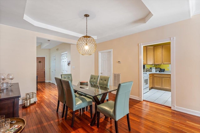 dining space with baseboards, a tray ceiling, visible vents, and light wood-style floors