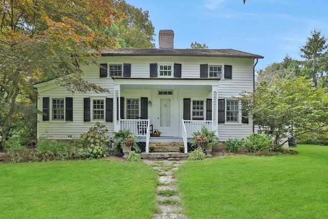 colonial house featuring covered porch, a chimney, and a front yard