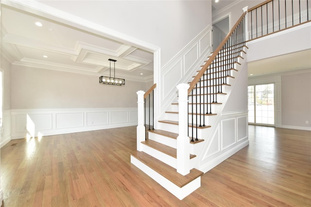 stairs featuring coffered ceiling, crown molding, and wood finished floors