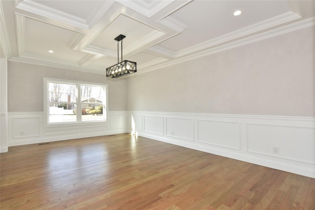 empty room featuring a chandelier, coffered ceiling, wood finished floors, and ornamental molding