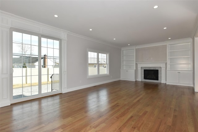 unfurnished living room with crown molding, a fireplace, built in shelves, and wood finished floors