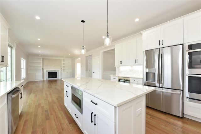 kitchen with decorative light fixtures, appliances with stainless steel finishes, open floor plan, white cabinetry, and a kitchen island