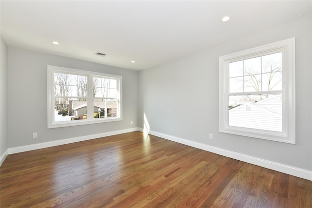 spare room with dark wood-style flooring, visible vents, and baseboards