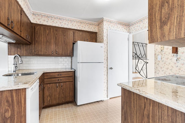 kitchen featuring white appliances, wallpapered walls, light stone counters, light floors, and a sink