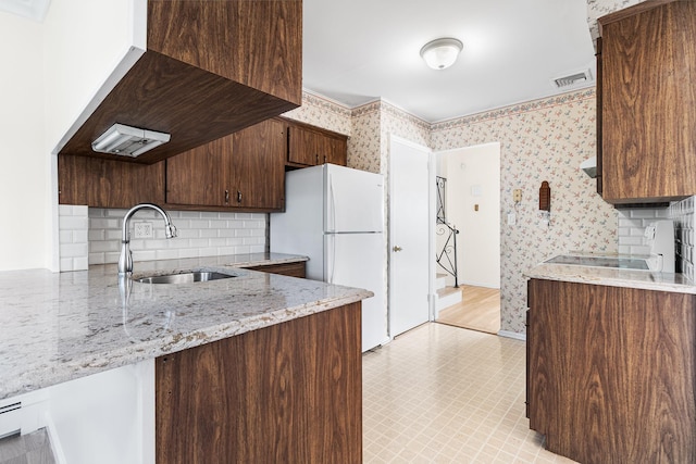 kitchen with a sink, visible vents, freestanding refrigerator, light stone countertops, and wallpapered walls