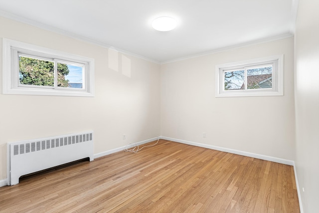 empty room with ornamental molding, radiator heating unit, plenty of natural light, and light wood-style floors