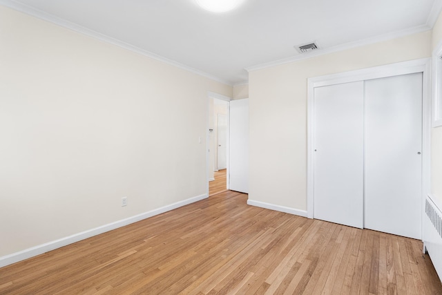 unfurnished bedroom featuring light wood finished floors, baseboards, visible vents, crown molding, and a closet