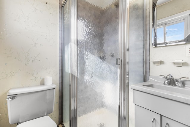 bathroom featuring toilet, wallpapered walls, vanity, and a stall shower