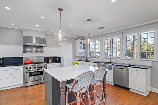 kitchen with visible vents, white cabinets, wall chimney exhaust hood, appliances with stainless steel finishes, and light wood-style floors