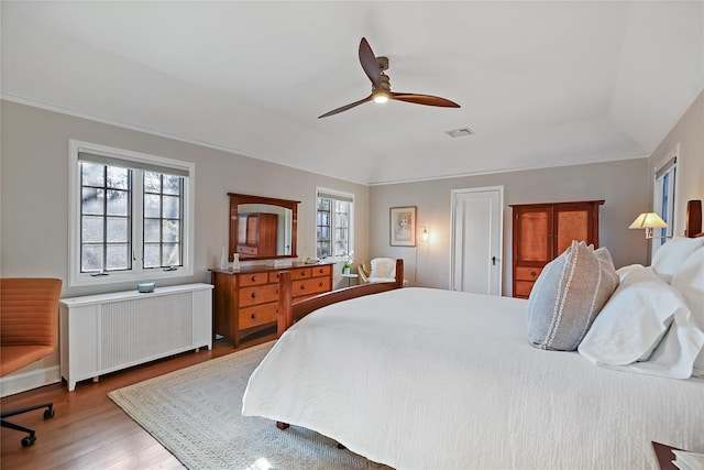 bedroom featuring lofted ceiling, radiator, visible vents, a ceiling fan, and wood finished floors