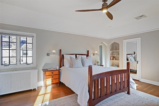 bedroom featuring baseboards, visible vents, radiator, ceiling fan, and wood finished floors