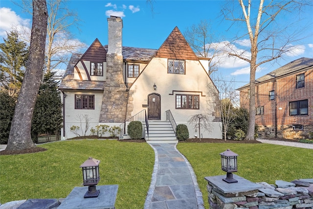 tudor home featuring a front yard, a chimney, and stucco siding