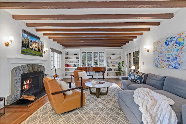 living area with beam ceiling, a lit fireplace, and wood finished floors