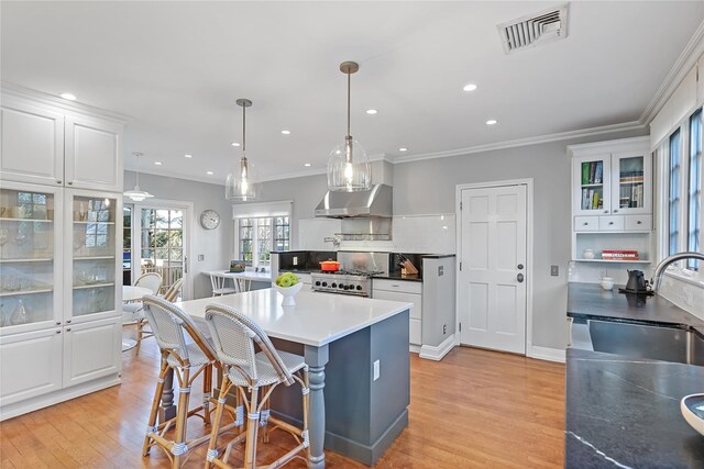 kitchen with visible vents, white cabinetry, a kitchen island, a sink, and under cabinet range hood