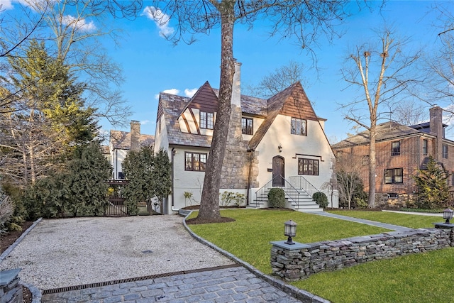 english style home featuring stucco siding, a front yard, a gate, a high end roof, and driveway