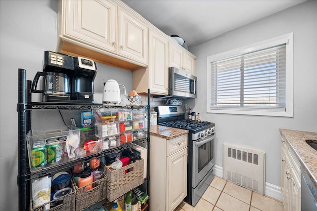 kitchen with appliances with stainless steel finishes, radiator, light stone counters, and light tile patterned floors