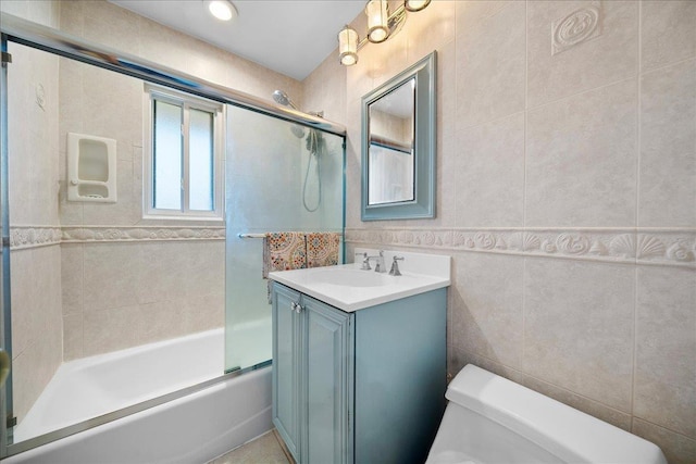 bathroom featuring toilet, shower / bath combination with glass door, tile walls, and vanity