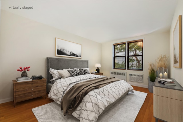 bedroom with baseboards, dark wood-type flooring, a wall unit AC, and radiator