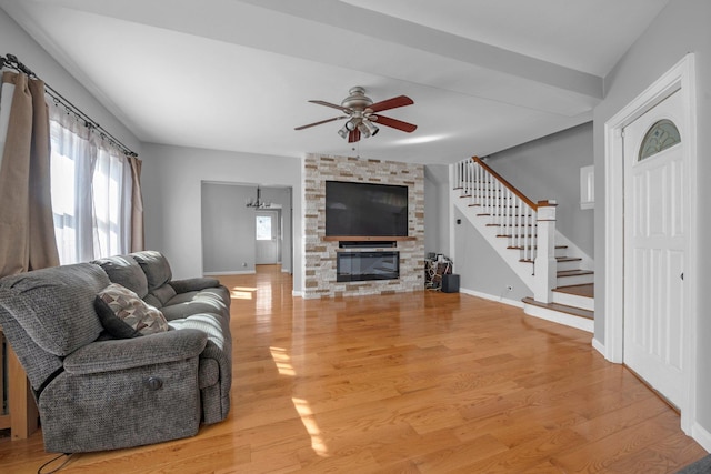 living area featuring light wood finished floors, baseboards, a ceiling fan, stairs, and a fireplace