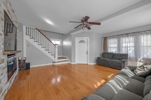 living area featuring stairs, a stone fireplace, wood finished floors, and a healthy amount of sunlight