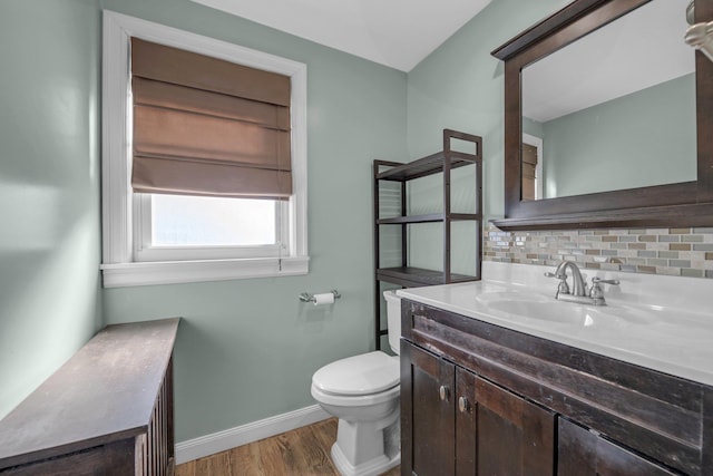 half bathroom featuring tasteful backsplash, toilet, vanity, wood finished floors, and baseboards