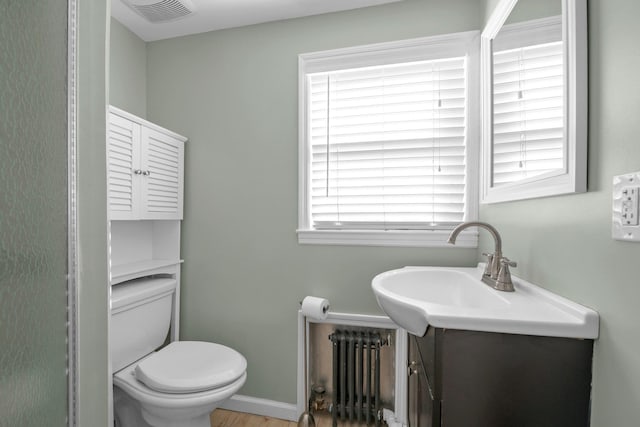 bathroom featuring toilet, vanity, visible vents, baseboards, and radiator heating unit