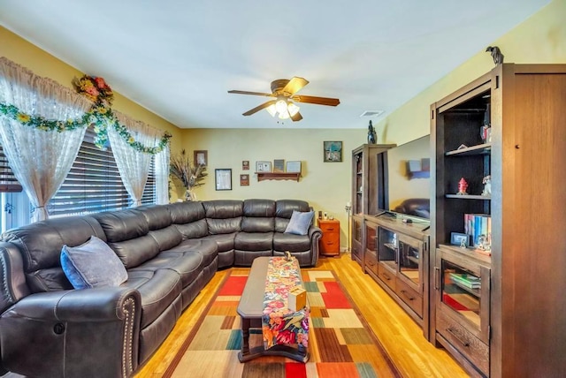 living area featuring visible vents, light wood finished floors, a ceiling fan, and a healthy amount of sunlight