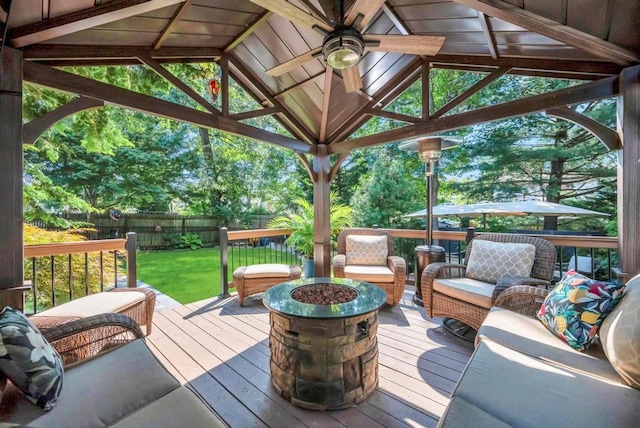 deck featuring a ceiling fan, an outdoor living space with a fire pit, a fenced backyard, a gazebo, and a yard