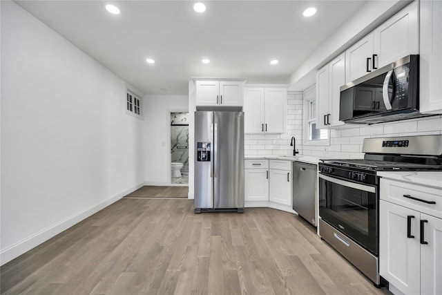 kitchen featuring tasteful backsplash, baseboards, appliances with stainless steel finishes, light wood-style floors, and white cabinetry