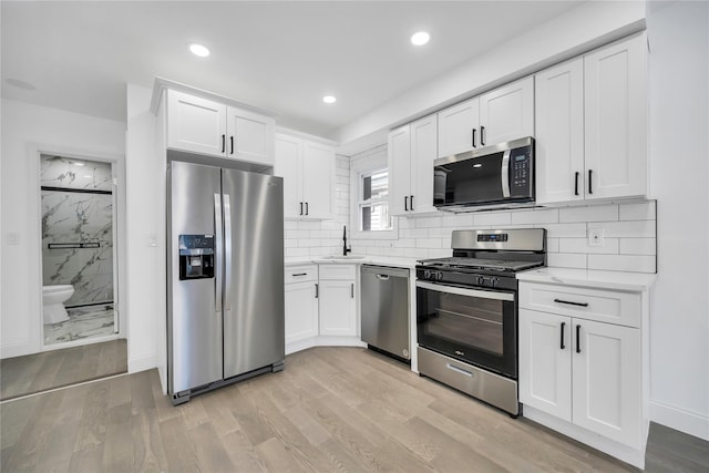 kitchen with light wood-style flooring, a sink, white cabinetry, appliances with stainless steel finishes, and decorative backsplash