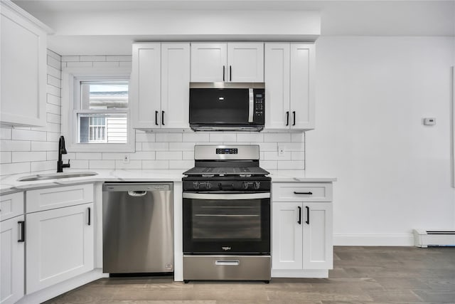 kitchen featuring stainless steel appliances, tasteful backsplash, baseboard heating, white cabinets, and a sink