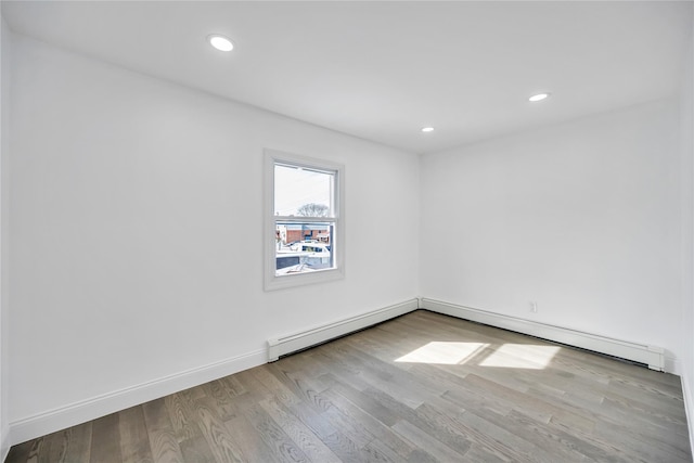 empty room featuring a baseboard heating unit, recessed lighting, baseboards, and wood finished floors