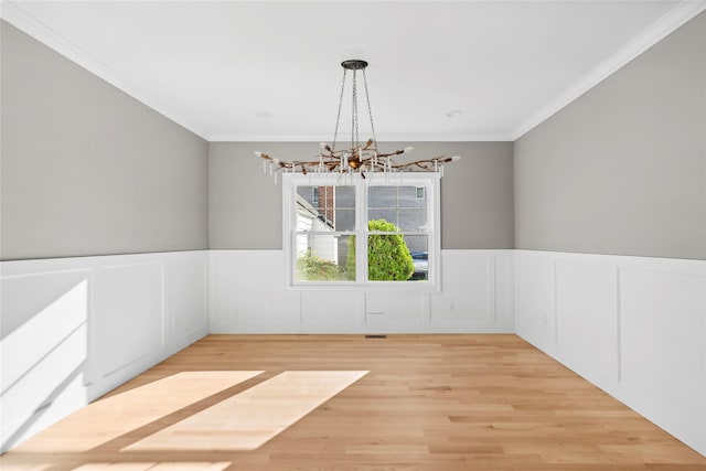 unfurnished dining area with a chandelier, ornamental molding, wainscoting, and light wood-style floors