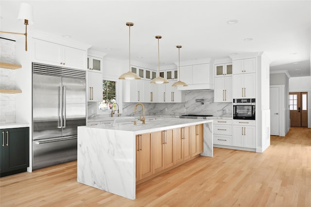 kitchen featuring built in fridge, decorative backsplash, a kitchen island with sink, crown molding, and black oven