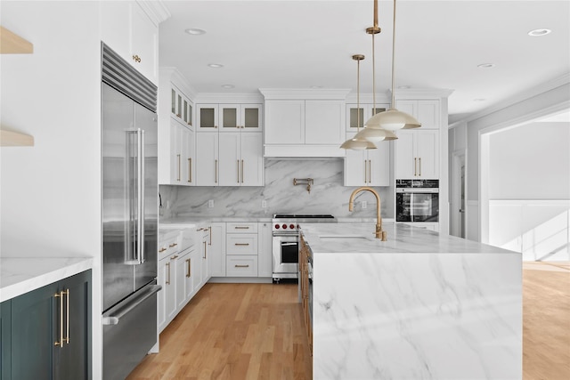 kitchen featuring premium appliances, decorative backsplash, a sink, and white cabinets