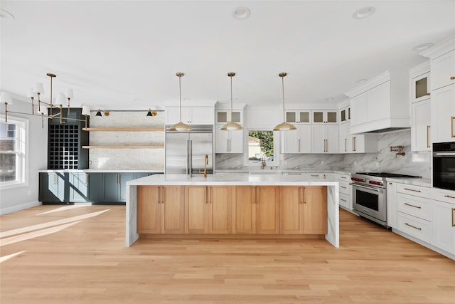 kitchen with premium appliances, a center island, light countertops, white cabinets, and a sink