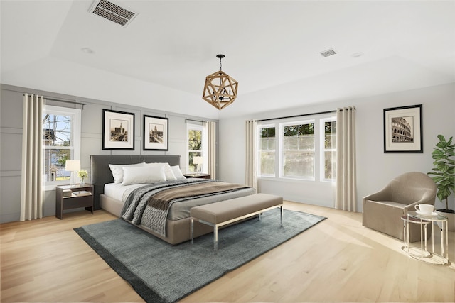 bedroom with light wood-type flooring, a raised ceiling, and visible vents