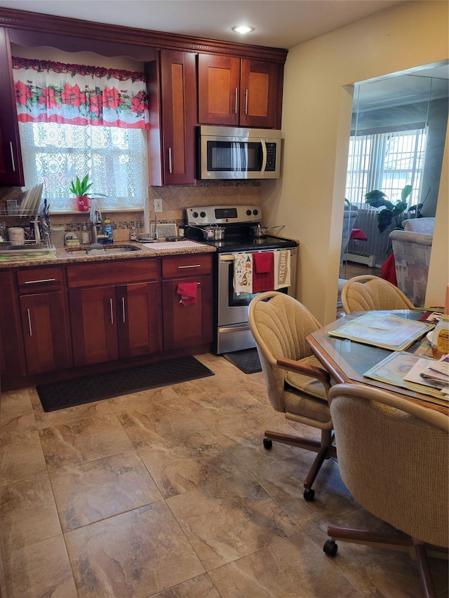 kitchen featuring stainless steel appliances, reddish brown cabinets, a sink, and decorative backsplash