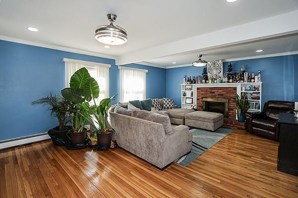 living room with ornamental molding, a brick fireplace, baseboard heating, and wood finished floors