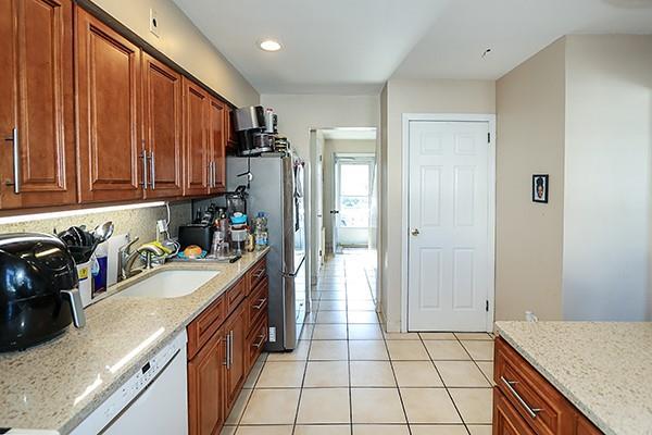 kitchen with light tile patterned floors, light stone counters, a sink, brown cabinets, and dishwasher