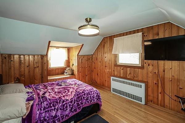 bedroom featuring lofted ceiling, radiator, wood walls, and light wood finished floors